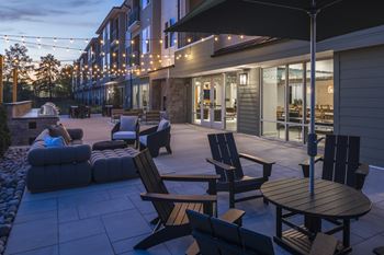 A patio with chairs and a table is lit up with string lights.